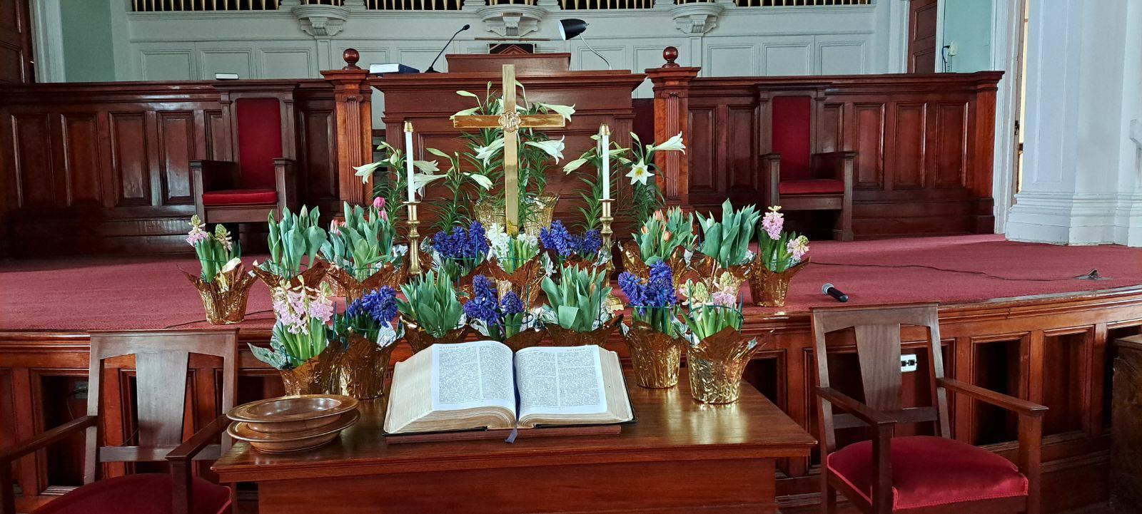 An altar in a church with open, and an open book with colorful floral arrangements.